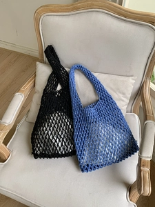 Detail of handmade crochet mesh tote bags in black and royal blue on a vintage wooden chair