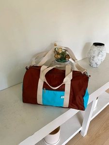 Detail view of large two-tone nylon tote bag with shoulder strap on a white bench