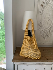 Detail of yellow hand-woven knit tote bag with honeycomb mesh pattern on vintage cabinet