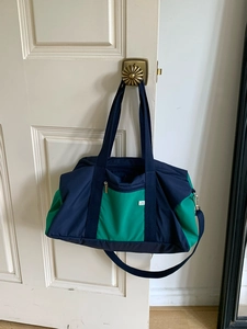Detail of color-block navy and green nylon tote bag hanging on a white wooden door