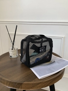 Black mesh travel storage bag with handle on a wooden table with home decor items