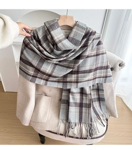 Detail of soft thick brown plaid scarf with long fringe tassels on beige wool coat