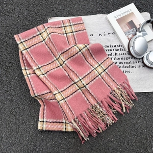 Pink plaid winter scarf with fringe tassels on a grey fabric base with lifestyle accessories