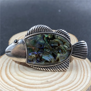 Macro shot of tropical fish brooch featuring colorful abalone shell and silver textured metal