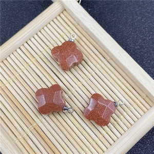 Detail of three clover-shaped red sandstone charms with silver rings on a bamboo tray