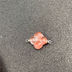 Macro detail of a carved pink quartz clover connector with metallic hanging loops