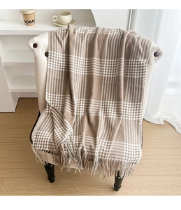 Detail of a vintage plaid scarf with tassels draped over a cozy minimalist sofa