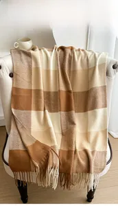 Detail of checkered plaid shawl with fringe draped on a sofa in a cozy indoor setting