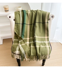 Detail of green plaid scarf with soft tassels draped on a white leather chair