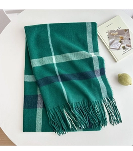 Close-up of thick green plaid scarf texture and fine tassels on a minimalist table