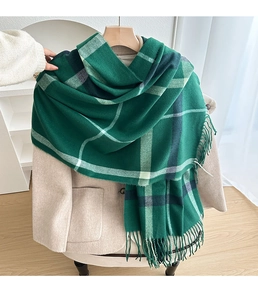 Detail of green plaid scarf with thick tassels hanging on a beige blazer and hanger