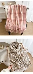 Detail view of plaid tassel scarves in soft pink and brown tones on a cozy white chair