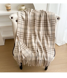 Detail of warm beige plaid scarf with soft fringe edges draped on a white chair