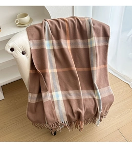 Close-up of brown plaid scarf with long tassels draped over a white chair in a warm room