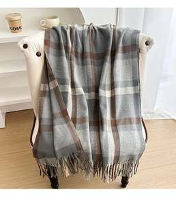 Close-up of thick plaid scarf with tassels on armchair, warm brown and grey checkered texture