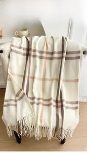 Detailed view of warm beige tartan cashmere-feel scarf with classic fringe on a chair