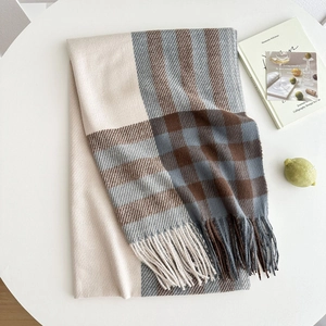 Thick plaid scarf with tassels in beige and grey, folded on a table for winter