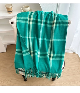 Detail of green plaid cashmere-feel scarf with long tassels draped on a white chair