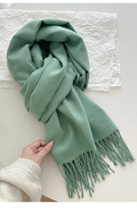 Close-up of sage green knit scarf showing soft texture and fringe tassel detail