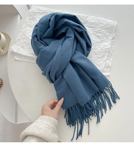 Close-up of soft dusty blue cashmere-like scarf with long fringe details on white background