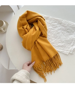 Detail of bright yellow fringed scarf on white desk with cozy lifestyle props