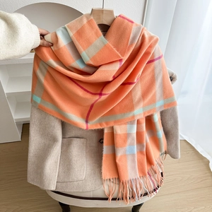 Thick checkered scarf in orange plaid with tassels draped over a beige wool coat