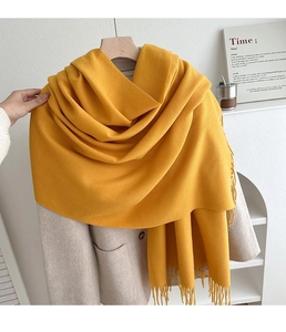 Close-up of ginger yellow cashmere-like scarf with long tassels on a beige coat