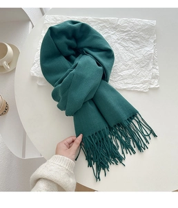 Detailed close-up of dark green cashmere-feel knit scarf with long decorative tassels