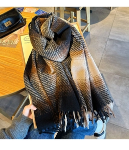 Detail of a thick plaid scarf with tassels in brown and black on a wooden table