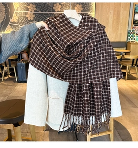 Dettaglio di una spessa sciarpa pied de poule con frange su un cappotto beige in un caffè