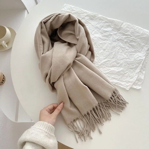 Oatmeal thick cashmere-feel scarf with fringe detail on a minimalist white table