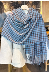 Detail of blue and brown plaid scarf with tassels styled on a cream wool coat