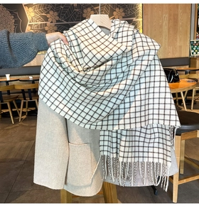 Close-up of black and white plaid scarf with fringe details on a beige wool coat