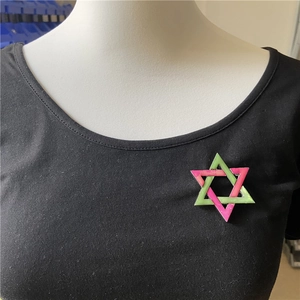 Detail showing hexagram brooch with pink and green gradient enamel on a black shirt