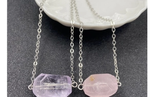 Macro view of faceted amethyst and rose quartz pendants on delicate silver necklaces