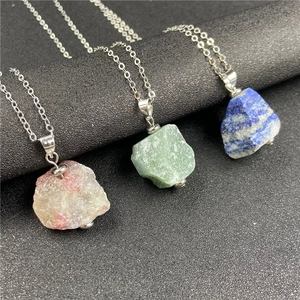 Detail of three natural raw gemstone pendants in purple, green, and blue on silver chains