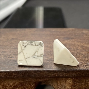 Dettaglio macro di orecchini quadrati in howlite con venature grigie su base in legno