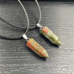 Close-up of hexagonal unakite crystal pendants on black cord over dark wood texture