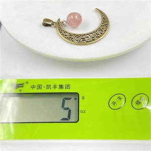Detail shot of moon pendant with pink crystal bead showing 5g weight on a scale