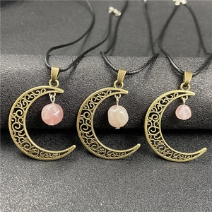 Macro detail of bronze hollow moon pendants with raw rose quartz stones on black surface