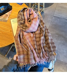 Detail of a thick plaid scarf with pink and brown checkers and tassel edges on a table