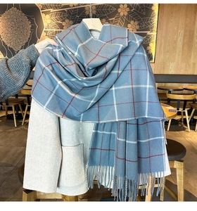 Détail de l'écharpe à carreaux bleus et pompons sur un manteau en laine beige au café