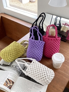 Détail de mini sacs seaux tricotés à la main en cinq couleurs posés sur une table en bois