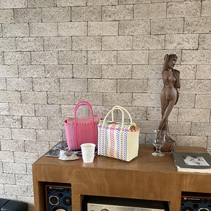 Détail de sacs paniers tressés en PVC rose et rayures colorées sur une table en bois