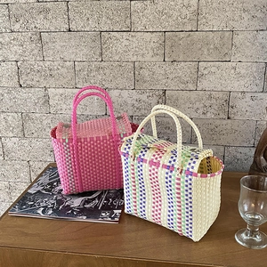 Détail de sacs cabas tissés en PVC rose et rayures multicolores sur table en bois