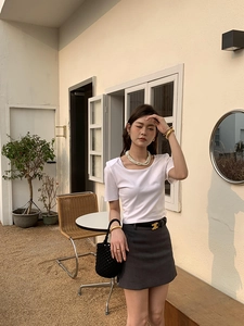 Style chic avec t-shirt blanc ajusté, mini-jupe anthracite et collier de perles décoratif