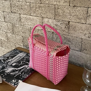 Détail d'un sac cabas tissé en PVC avec motif contrasté rose vert et boucles métalliques