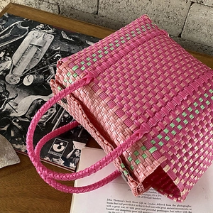 Sac panier tissé en PVC rose et vert posé sur une table en bois rustique