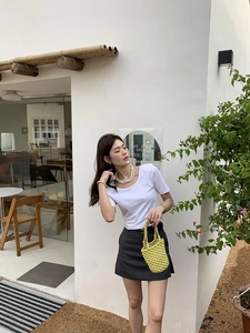 Détail du sac seau tissé main jaune avec t-shirt blanc et jupe grise en extérieur