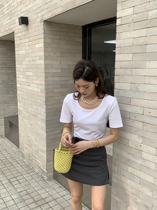 Détail d'un sac seau tressé jaune vif avec un t-shirt blanc et une jupe grise courte